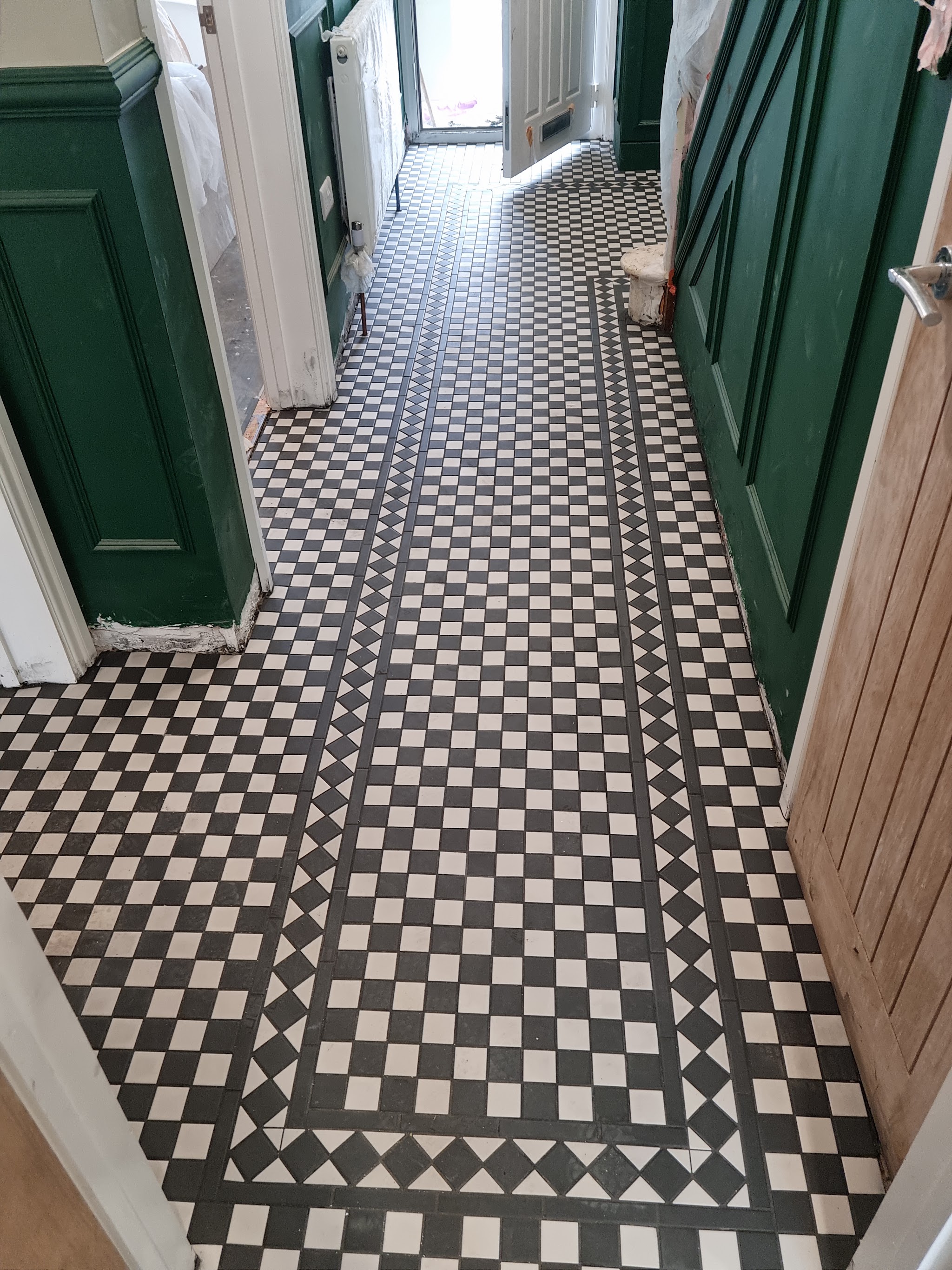 Black and white mosaic tiled hallway floor with a bordered pattern, between green panelled walls