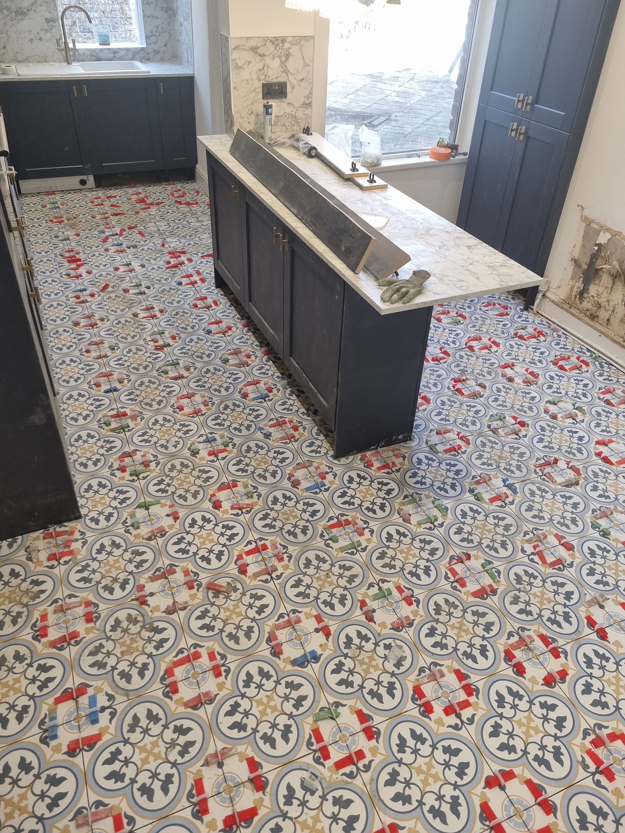 Patterned floor tiles being laid in a kitchen, with levelling clips still in place