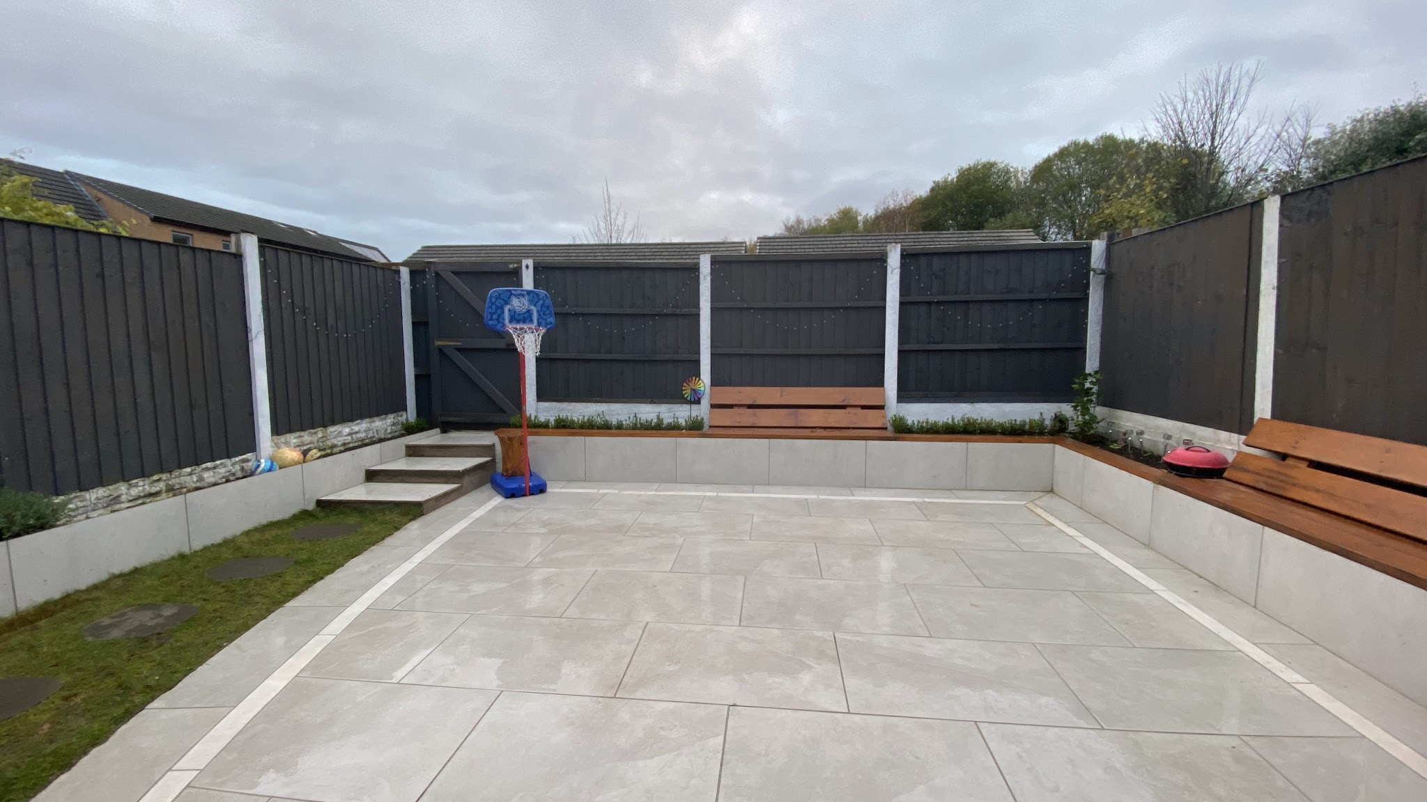 Light porcelain patio with tiled steps, a raised border and tiled seating walls against dark fencing