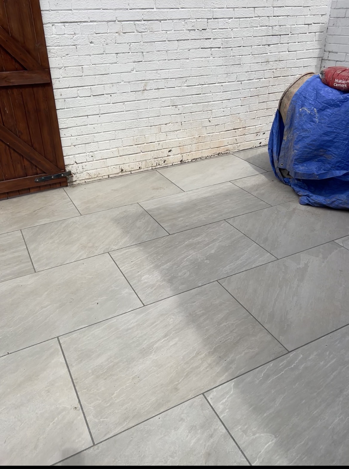 Large-format grey porcelain floor laid against a white brick wall